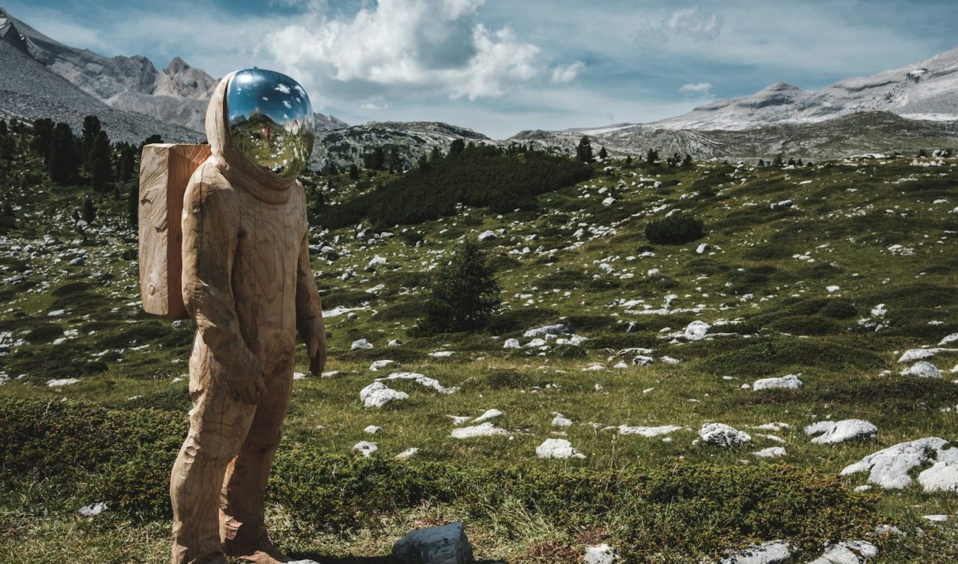 Astronaut im Raumanzug steht auf einer grünen Wiese mit Bergen und Wolken im Hintergrund.
